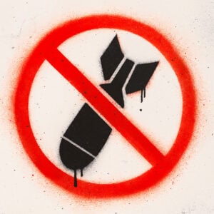 Pochoir représentant une bombe noire barrée d’un trait rouge dans un cercle rouge, symbole percutant de protestation contre la guerre, réalisé dans un style street art avec des coulures de peinture.