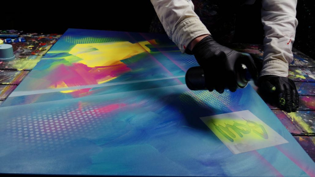 Auftragen von Sprühfarbe mit einer Schablone, um den Hintergrund des Kunstwerks Art is My Revolt zu strukturieren