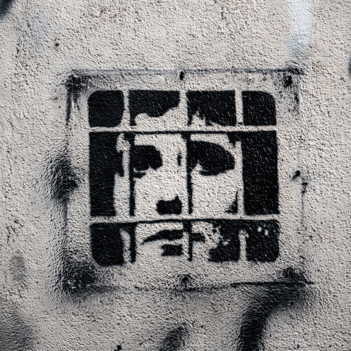 Stencil prigioniero applicato con spray nero su muro di cemento, mostrando un volto frammentato dietro le sbarre